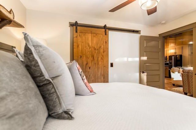 bedroom featuring a ceiling fan, a barn door, and black refrigerator with ice dispenser