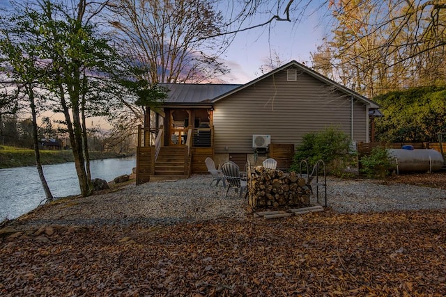 back of property at dusk with stairway, a water view, and metal roof