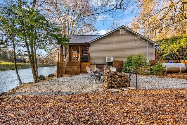 back of property featuring stairs, a water view, and metal roof