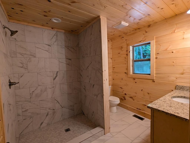 bathroom with a tile shower, wood walls, vanity, wood ceiling, and toilet