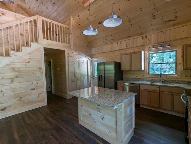 kitchen with appliances with stainless steel finishes, wooden walls, sink, a center island, and light stone counters