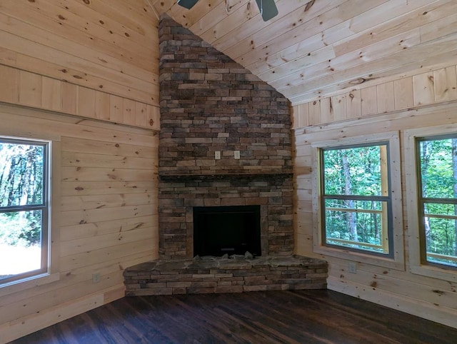 unfurnished living room featuring lofted ceiling, a stone fireplace, wood-type flooring, and wooden walls