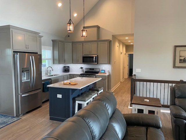 kitchen with sink, a breakfast bar, appliances with stainless steel finishes, hanging light fixtures, and a kitchen island