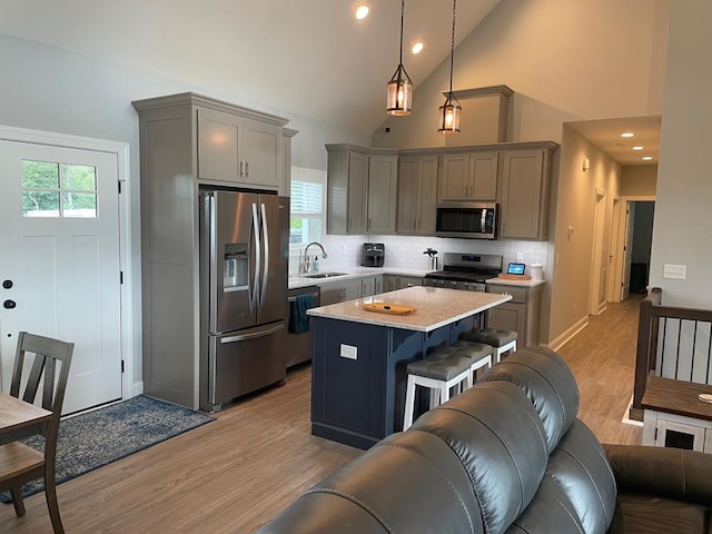 kitchen featuring sink, appliances with stainless steel finishes, hanging light fixtures, a center island, and light wood-type flooring