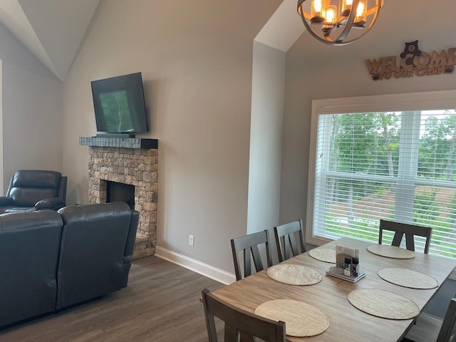 dining room featuring a notable chandelier, wood-type flooring, lofted ceiling, and a stone fireplace