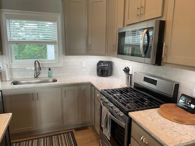 kitchen featuring stainless steel appliances, light stone countertops, sink, and gray cabinets