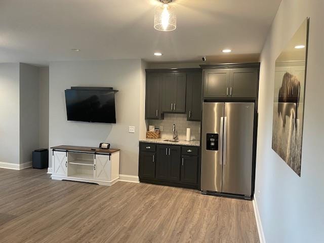 kitchen with sink, stainless steel fridge, backsplash, light stone counters, and wood-type flooring