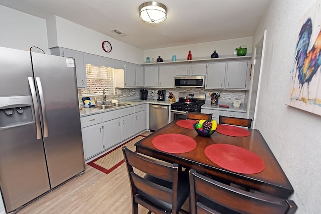 kitchen featuring appliances with stainless steel finishes, tasteful backsplash, gray cabinetry, sink, and light hardwood / wood-style flooring