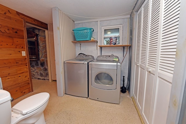 laundry room featuring wooden walls, washer and dryer, and a textured ceiling