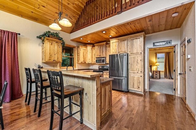 kitchen featuring wooden ceiling, dark wood-style floors, appliances with stainless steel finishes, a breakfast bar area, and a peninsula