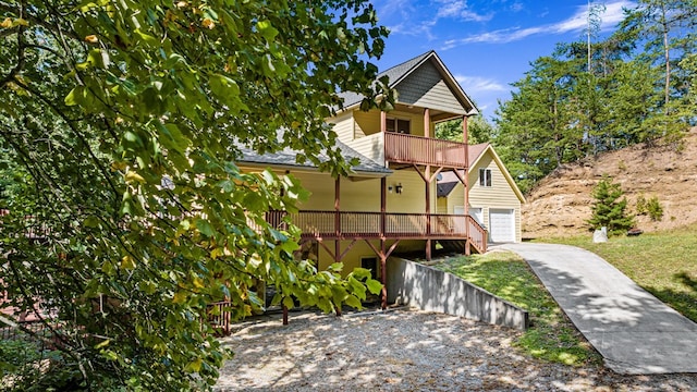 view of front of home with a balcony, driveway, a garage, and an outbuilding