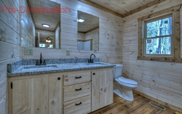 bathroom featuring wood finished floors, visible vents, double vanity, a sink, and toilet