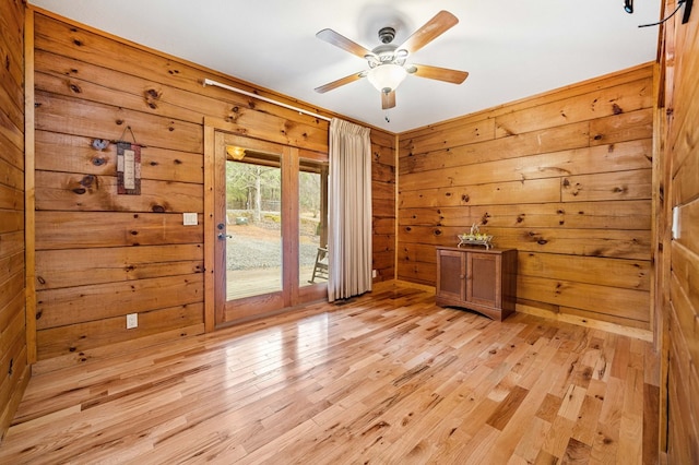 empty room featuring ceiling fan, wooden walls, and light hardwood / wood-style floors