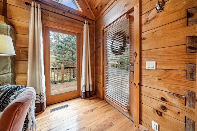 doorway to outside with light wood-type flooring, lofted ceiling, and wooden walls