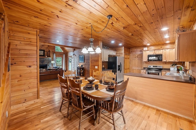 dining space with sink, light wood-type flooring, a fireplace, wooden walls, and wood ceiling