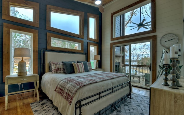 bedroom featuring a towering ceiling, hardwood / wood-style floors, wooden walls, and access to outside