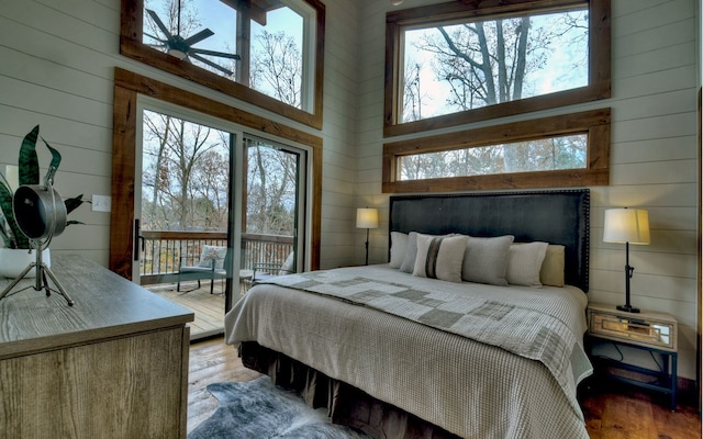 bedroom featuring a high ceiling, hardwood / wood-style floors, wooden walls, and a fireplace