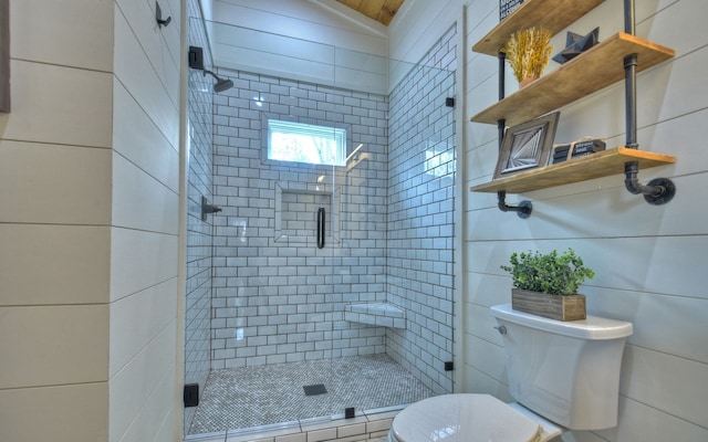 bathroom featuring lofted ceiling, a shower with shower door, toilet, and tile walls