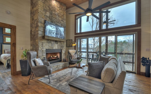 living room featuring high vaulted ceiling, ceiling fan, hardwood / wood-style flooring, and a stone fireplace