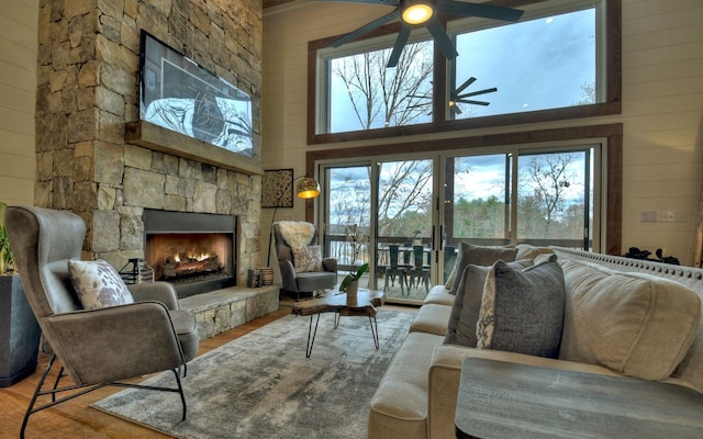 living room with a fireplace, wooden walls, wood-type flooring, ceiling fan, and a towering ceiling