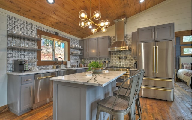 kitchen with a kitchen island, vaulted ceiling, light stone countertops, wall chimney exhaust hood, and stainless steel appliances