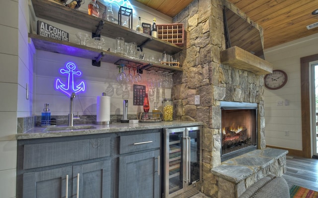 bar featuring wine cooler, sink, a stone fireplace, wooden ceiling, and hardwood / wood-style flooring