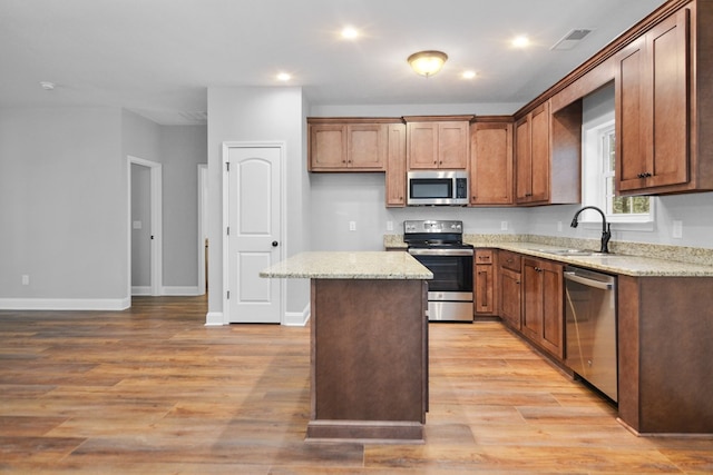 kitchen featuring sink, light stone counters, a center island, light wood-type flooring, and appliances with stainless steel finishes