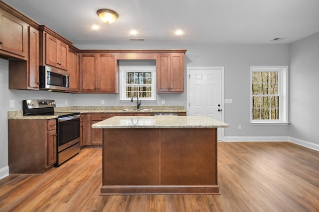 kitchen featuring stainless steel appliances, a center island, sink, and light stone countertops