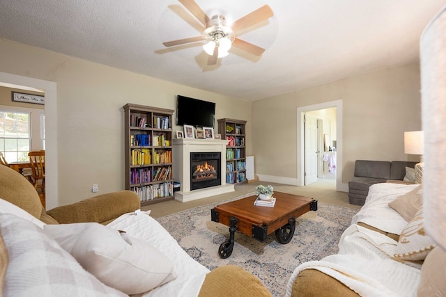living room featuring carpet flooring, a ceiling fan, a glass covered fireplace, a textured ceiling, and baseboards