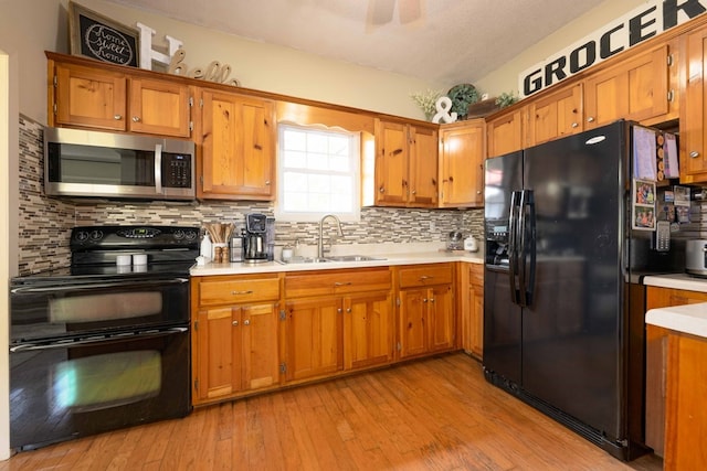 kitchen with light countertops, a sink, light wood finished floors, brown cabinetry, and black appliances