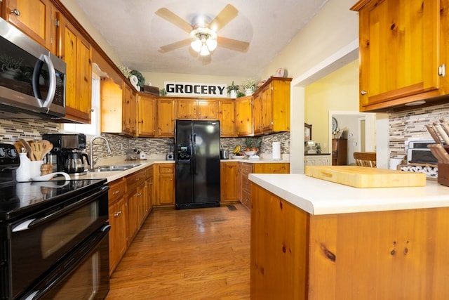 kitchen with light countertops, a sink, brown cabinetry, black appliances, and ceiling fan
