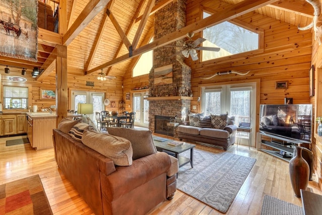 living room featuring light wood-type flooring, wooden walls, a stone fireplace, and beam ceiling