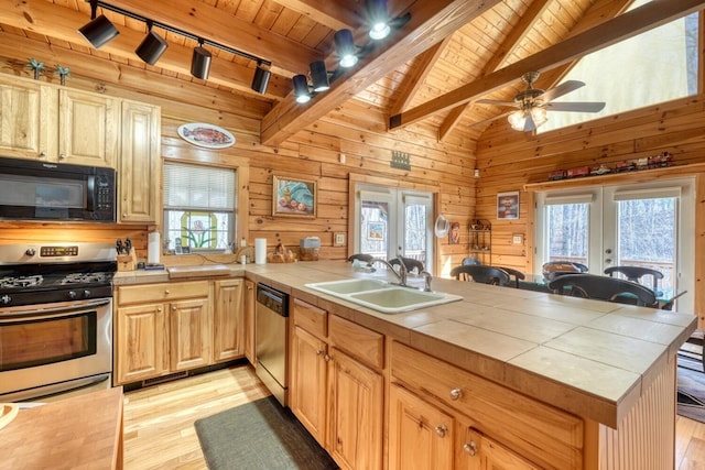 kitchen featuring appliances with stainless steel finishes, sink, wood walls, french doors, and tile countertops