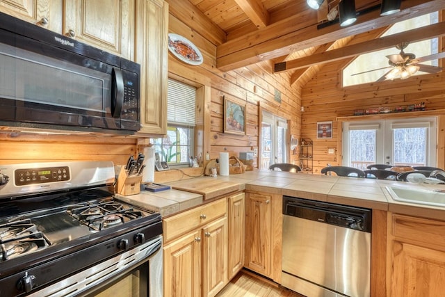 kitchen featuring appliances with stainless steel finishes, sink, tile countertops, and wooden walls