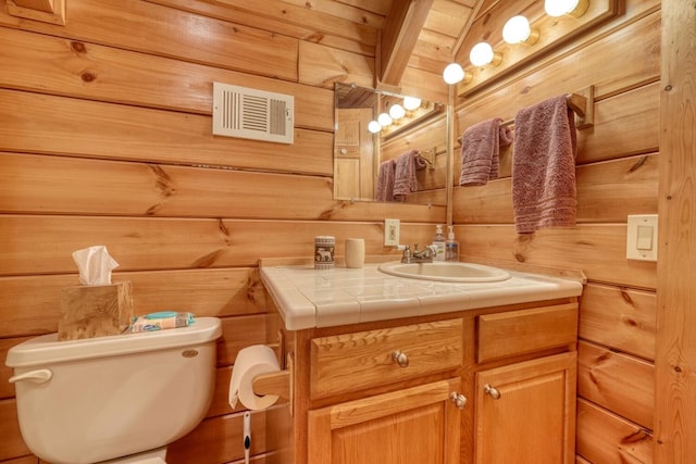 bathroom featuring toilet, wood walls, and vanity