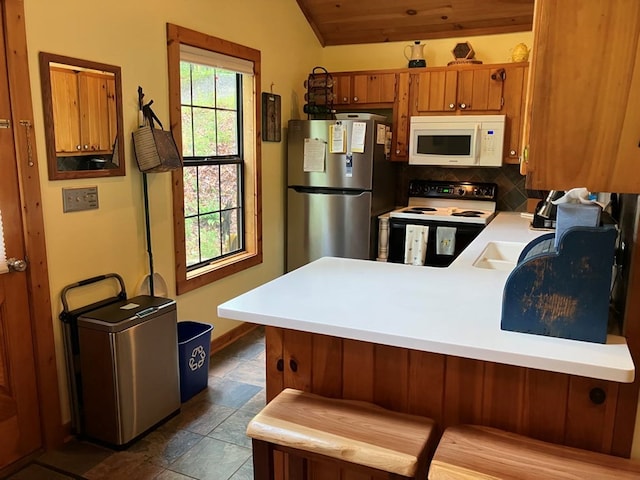 kitchen with white microwave, range with electric cooktop, freestanding refrigerator, brown cabinets, and light countertops