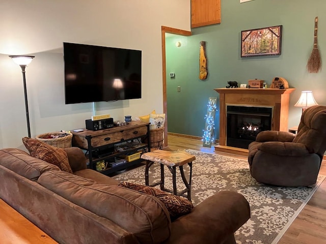 living area with wood finished floors, a warm lit fireplace, and baseboards