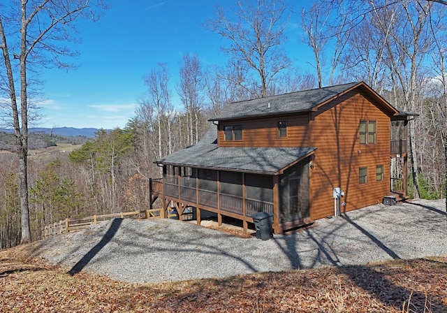 rear view of property with driveway, a shingled roof, and a sunroom