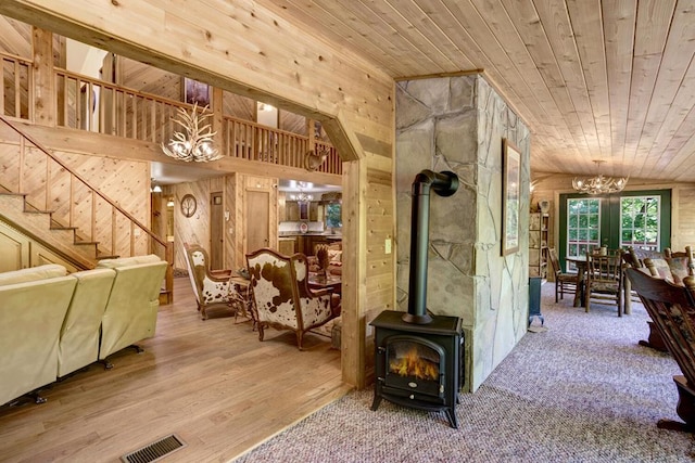 interior space featuring a chandelier, a wood stove, vaulted ceiling, wood walls, and wooden ceiling