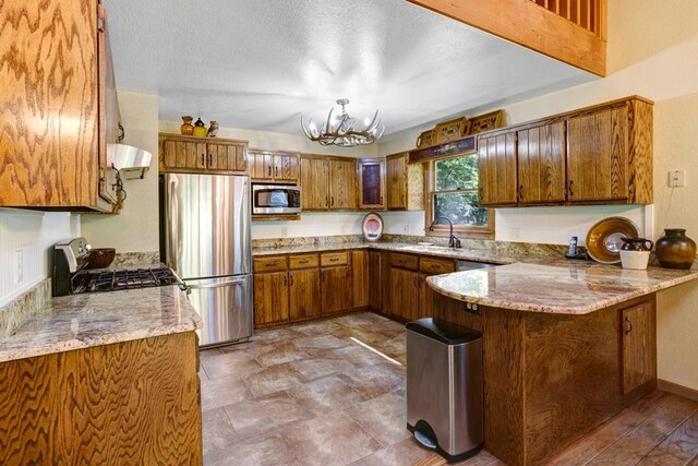 kitchen featuring sink, kitchen peninsula, ventilation hood, appliances with stainless steel finishes, and a notable chandelier