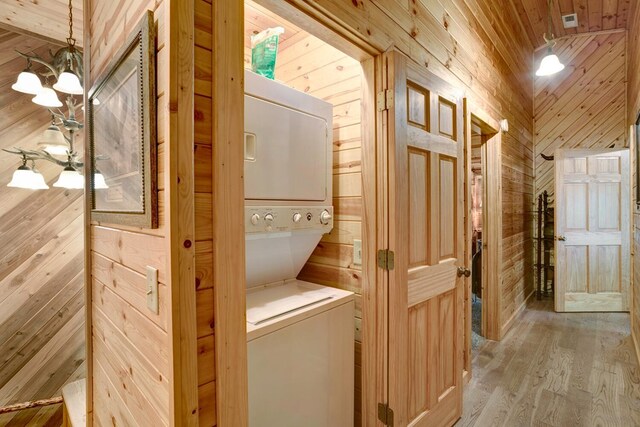 laundry area with wooden ceiling, stacked washer and clothes dryer, light hardwood / wood-style floors, and wooden walls