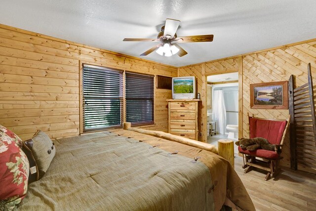 bedroom featuring multiple windows, connected bathroom, ceiling fan, hardwood / wood-style flooring, and wooden walls