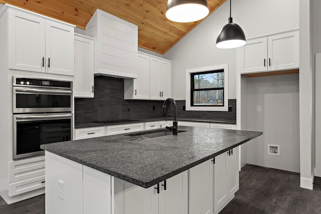 kitchen with double oven, sink, white cabinetry, and an island with sink