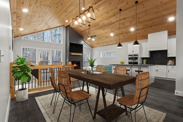 dining room featuring high vaulted ceiling, a fireplace, ceiling fan, wood ceiling, and dark wood-type flooring