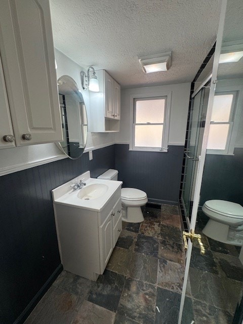 full bath with vanity, a stall shower, wainscoting, a textured ceiling, and toilet