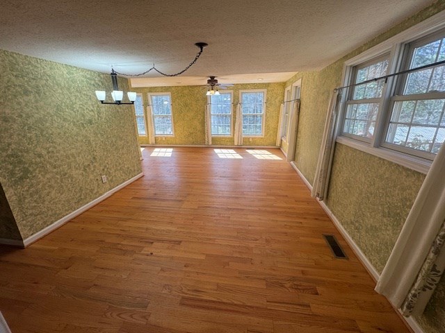 unfurnished dining area featuring a healthy amount of sunlight, wallpapered walls, and wood finished floors