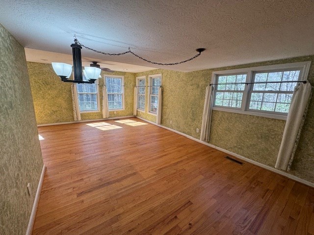 unfurnished dining area featuring visible vents, wallpapered walls, an inviting chandelier, wood finished floors, and a textured ceiling