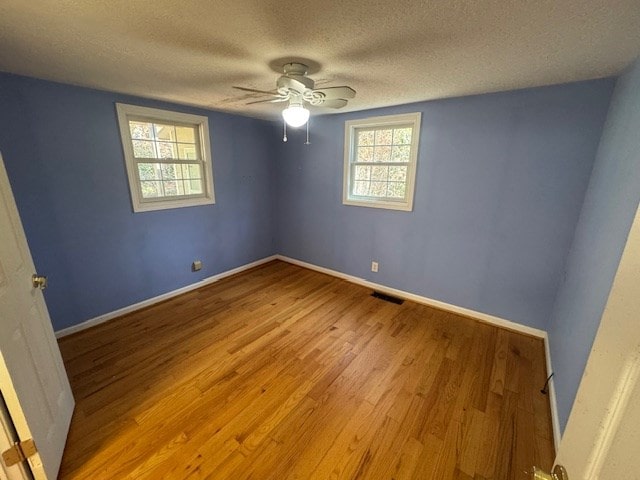 spare room featuring visible vents, baseboards, wood finished floors, a textured ceiling, and a ceiling fan