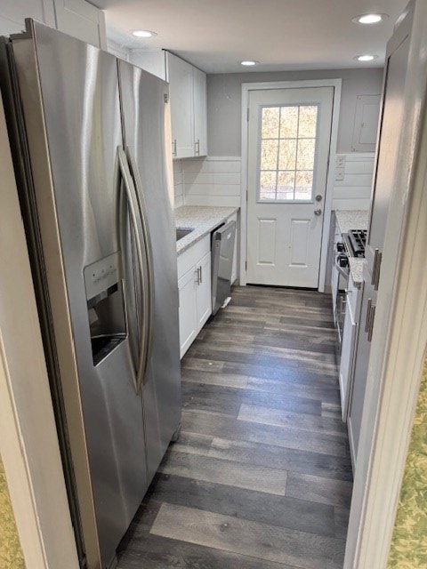 kitchen with light stone countertops, dark wood finished floors, white cabinets, appliances with stainless steel finishes, and backsplash