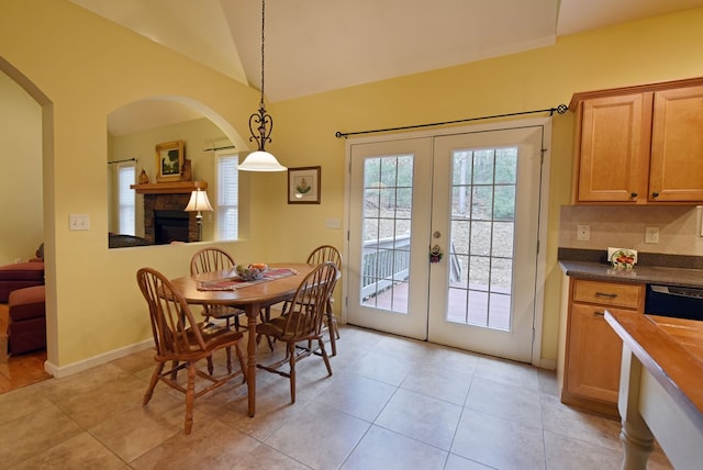 dining area featuring a stone fireplace, lofted ceiling, light tile patterned floors, and french doors